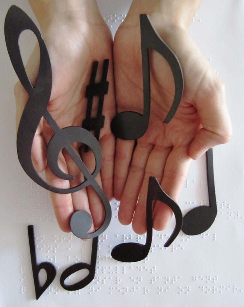Sobre un text en braille hi ha unes mans que unes mans que sostenen una clau de sol i diferents notes musicals