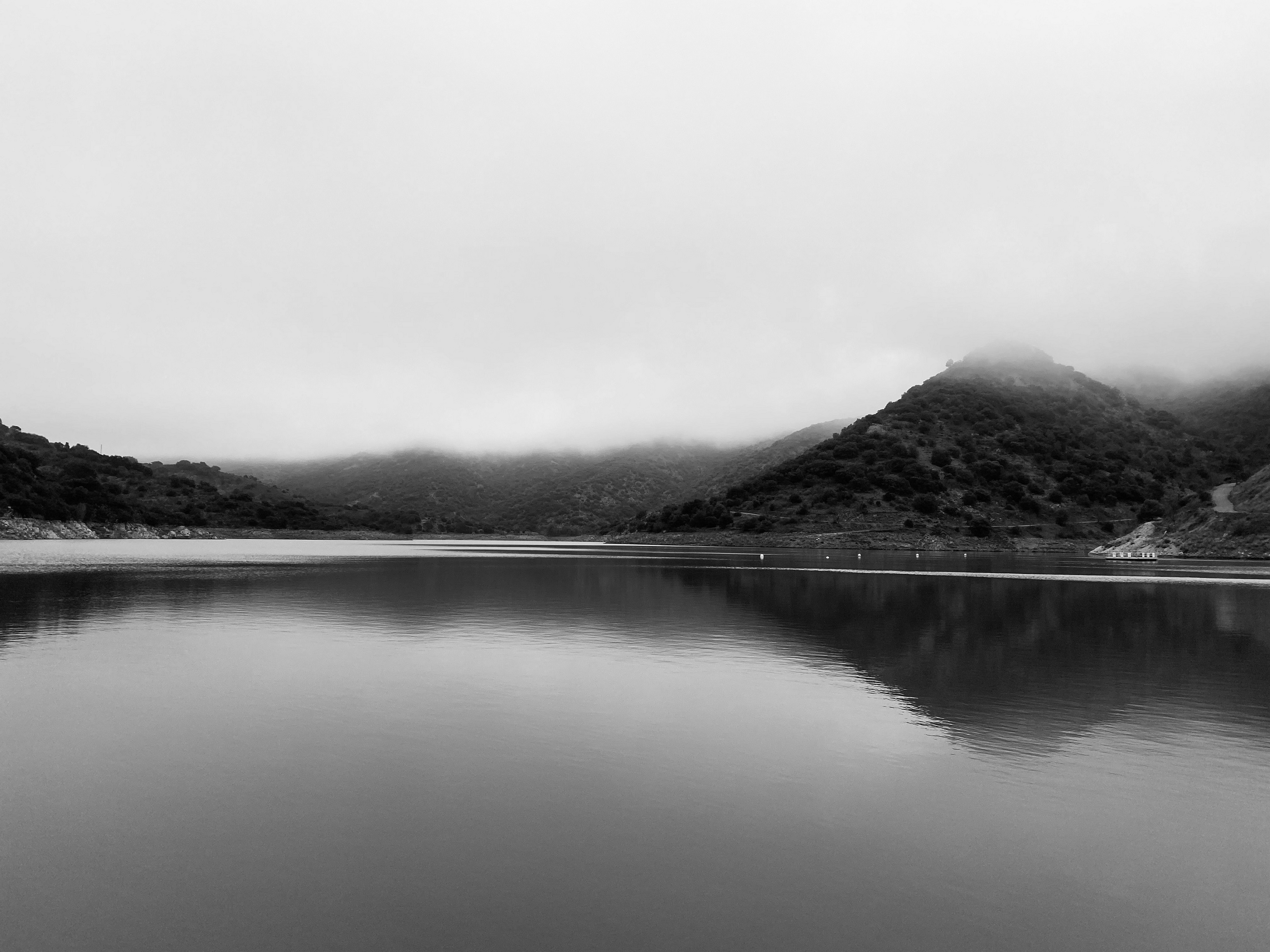 Imatge en blanc i negre d'un llac, amb un cel amb boira