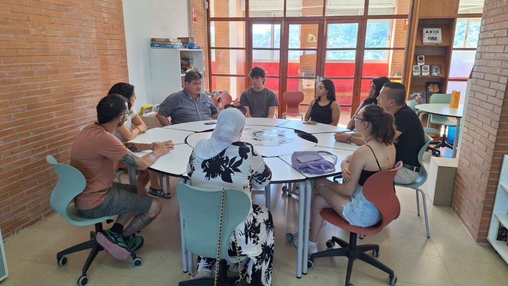 Primera trobada de la xarxa AlumniFP La Bastida, amb una imatge de grup on apareixen exalumnes de l'institut, el director i la coordinadora pedagògica compartint la jornada. Seuen al voltant d'una taula rodona a la biblioteca del centre.