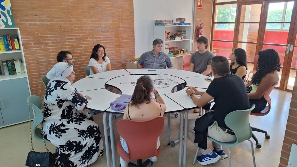 Primera trobada de la xarxa AlumniFP La Bastida, amb una imatge de grup on apareixen exalumnes de l'institut, el director i la coordinadora pedagògica compartint la jornada. Seuen al voltant d'una taula rodona a la biblioteca del centre.