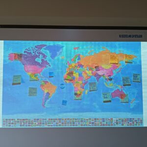 Mapa polític del món projectat en una pissarra, amb diferents postits enganxats per tots els continents, amb missatges escrits a mà (no es llegeix bé, per la distància).