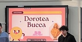Es veu una pantalla digital il·luminada amb una presentació sobre Dorotea Bucca. Un nombrós grup d'alumnes observen la pantalla mentre 3 alumnes en presenten el contingut.